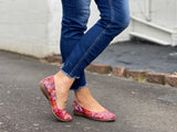 A person wearing blue jeans and red ballet flats with a multicolored design on the shoe's surface. Comfortable European women's shoes.