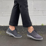 Person wearing Tango's gray brogues with white soles on a pavement against a gray wall. Comfortable, quality footwear. Great shoes!