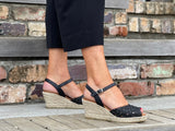 Black Viguera Volco sandals with a floral woven detail and an ankle strap with a buckle closure. The sandals have a natural woven jute wedge sole. Quality and comfortable European sandals.