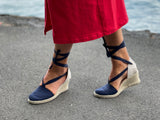 A person wearing Via Nova Flynn sandals in navy blue color. European Espadrille women's sandals with enclosed heel and toe. Woven wedge heel, lace up straps. Comfortable footbed. Made in Spain.